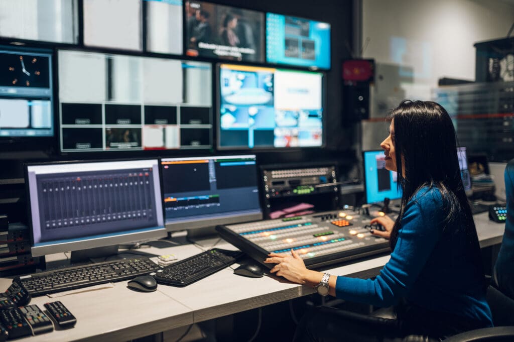 Middle aged woman TV editor working with vision mixer in a television broadcast room. TV engineer at editor in studio. Vision mixing panel in a television studio.